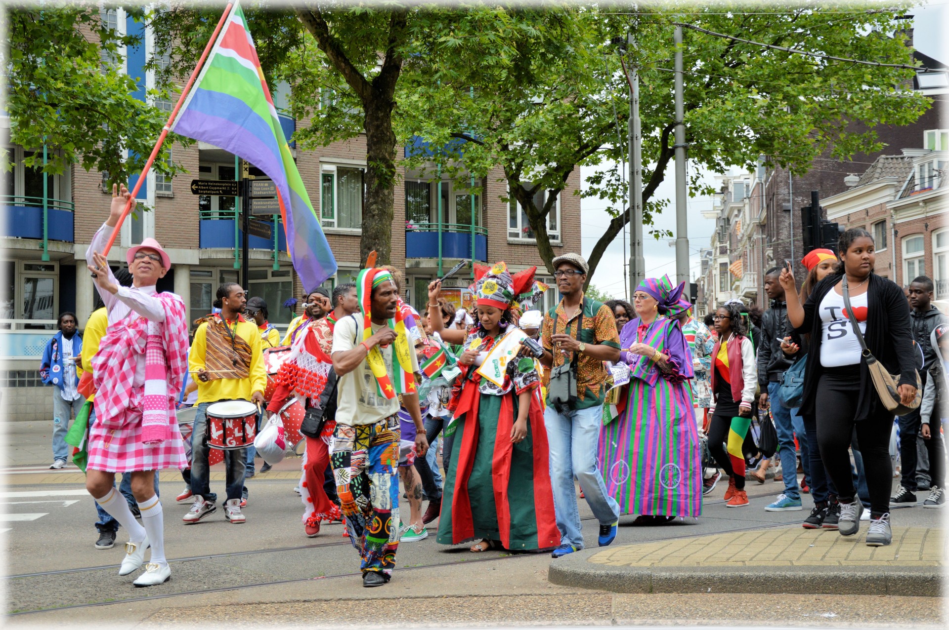 groep mensen loopt door de stad bij herdenking keti koti met vlaggen en in kleurrijke kleding