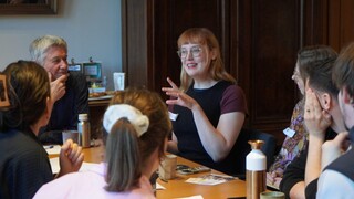 Vrouw spreekt met andere mensen aan een tafel 