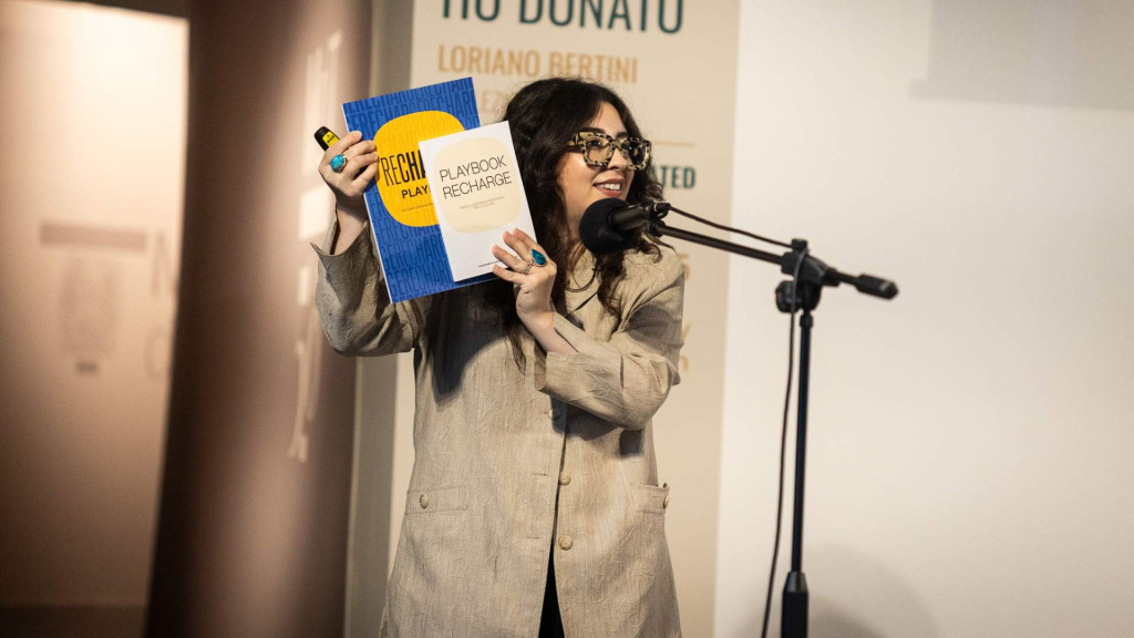 Vrouw met lang haar voor een microfoon presenteert een boek