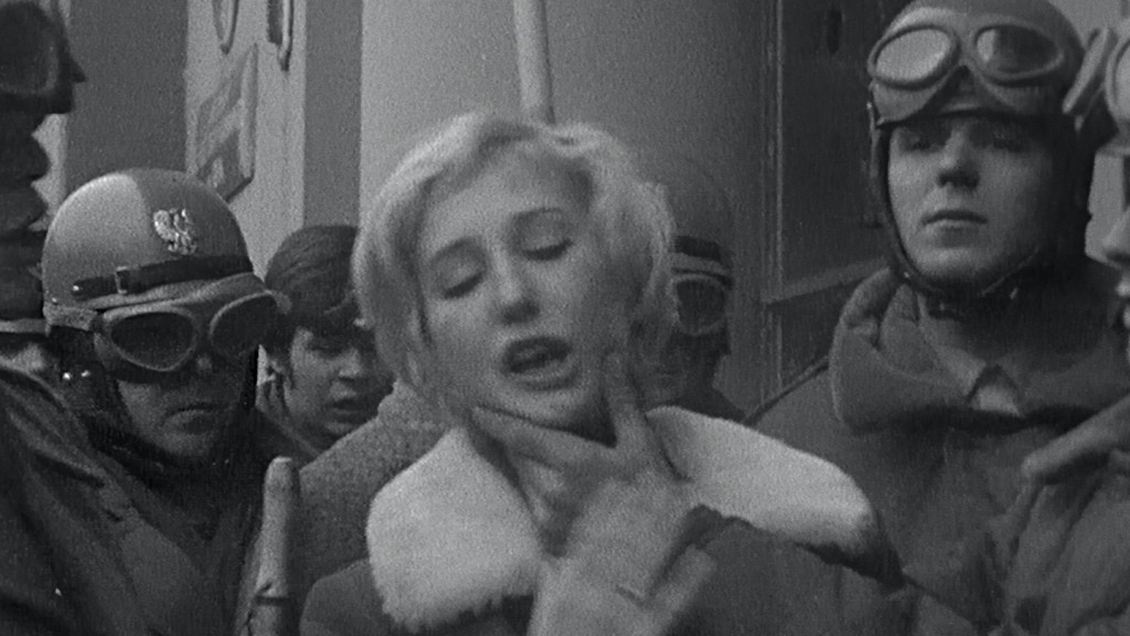 Zwartwitfoto van blonde vrouw omringd door gehelmde mannen, die haar gezicht vastpakken.