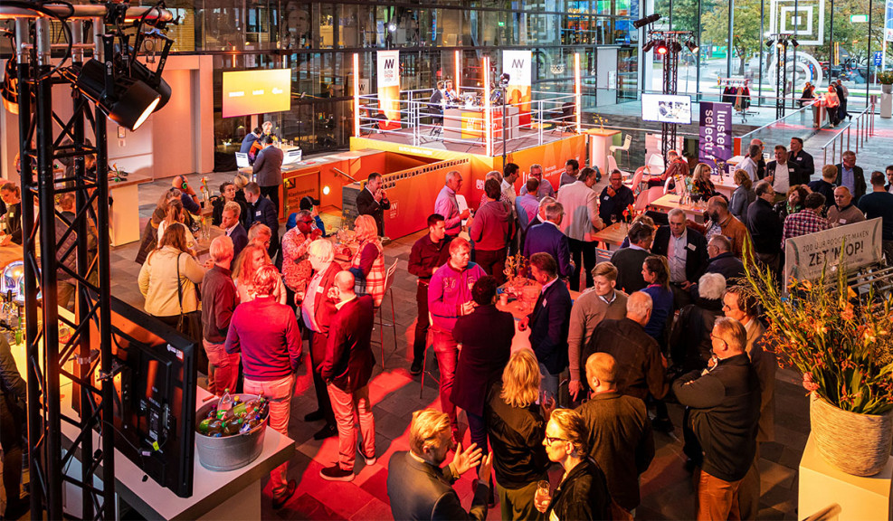 Sfeerbeeld van een vol atrium bij Beeld & Geluid. Centraal in de hal staat een podium waar podcast gemaakt wordt.