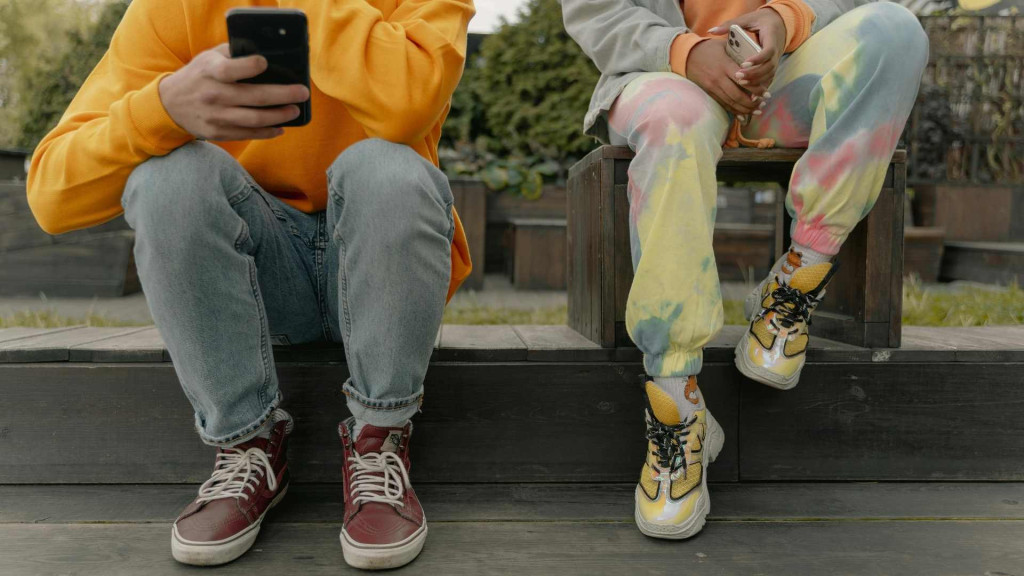 Jongeren zit met een telefoon op stoepje, je ziet alleen benen
