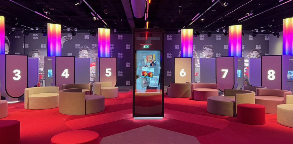 Tune-in ruimte van het museum met een paal in het midden waar een scherm aan vast zit en daar omheen tien persoonlijke zithoekjes die genummerd zijn