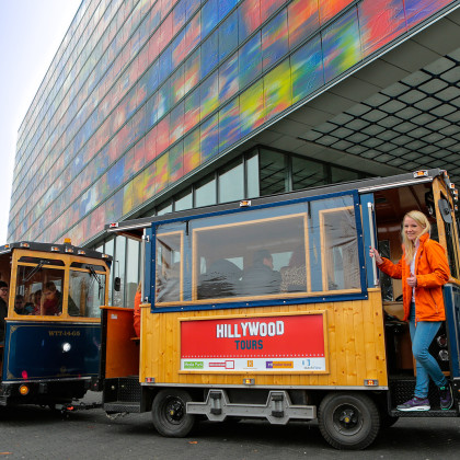 Hillywoodtours treintje bij de ingang van Beeld & Geluid. de conducteur hangt half uit het treintje terwijl de trein stilstaat.