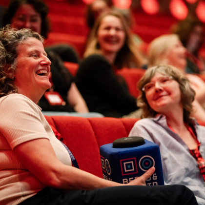 Twee vrouwen in het publiek in en zaal met microfoon in de hand