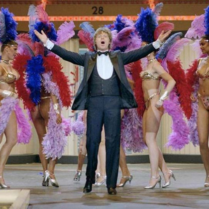 Willem Ruis staat op het podium, hij heeft ongeveer 8 show girls op de achtergrond terwijl het het publiek enthousiast tegemoet komt.